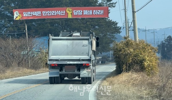 남향석산 인근 현산면 상구시 마을에 현수막 아래로 대형 덤프 차량이 지나고 있다.